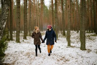 A couple walks hand in hand through a snow-covered forest, expressing joy and togetherness.