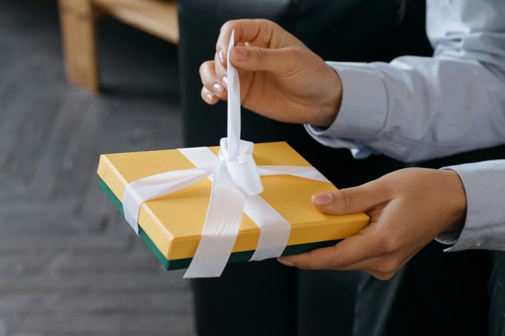 Close-up of hands untying a yellow gift box with a white ribbon indoors.