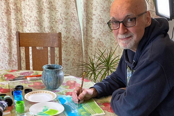 Man in glasses painting at a table at home