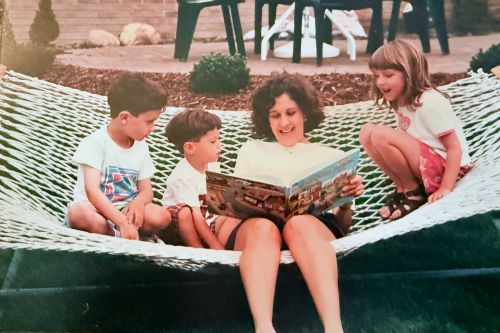 Mom with two sons and another little girl sitting on a hammock, mom reading them a book