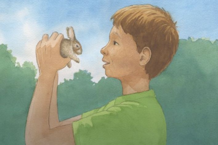 a boy holds up a small rabbit to look at it eye to eye, shrubs and sky behing them
