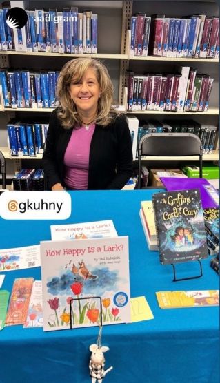 Woman sitting at her author table at the Ann Arbor Community Bookfest with her book, How Happy Is a Lark?