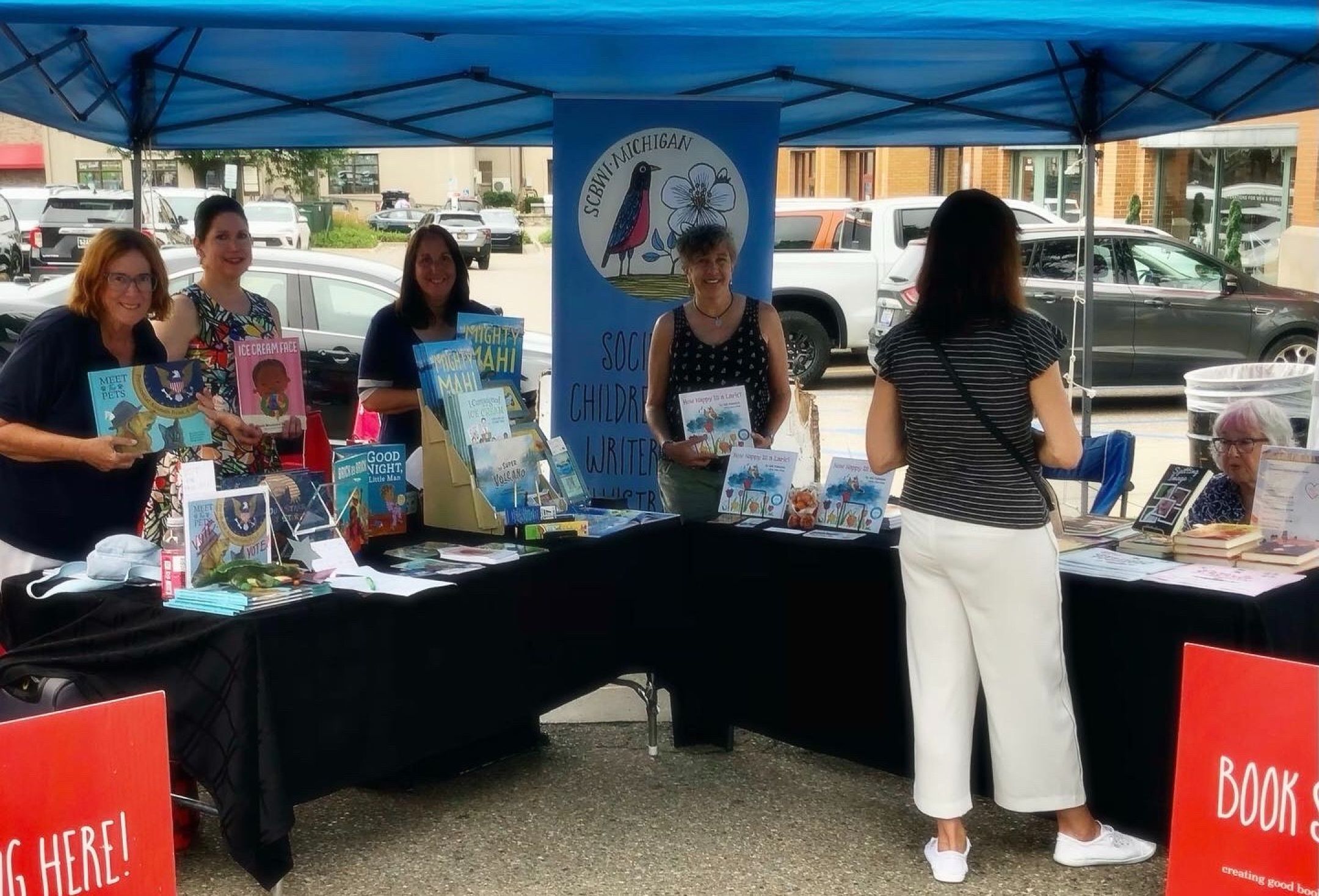 Group of authors with their books at tables under a tent