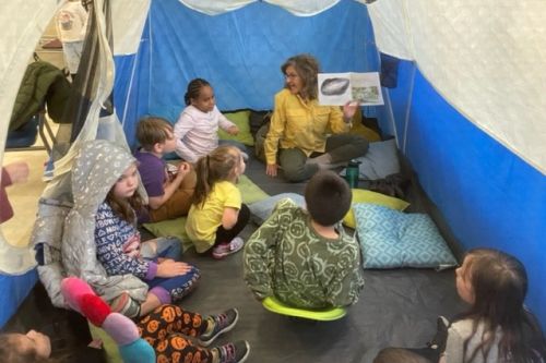 Gail Kuhnlein reading How Happy Is a Lark inside a tent to a group of children at Literacy Night