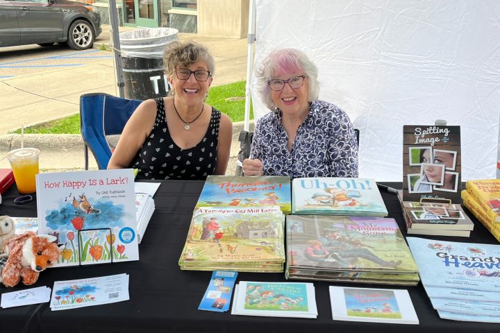 Two authors smiling at a table with their books