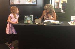 Gail signing a book and a little girl looking on