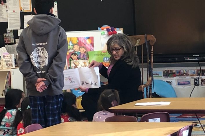 Gail reading her book to five young girls wearing pajamas and a boy, standing